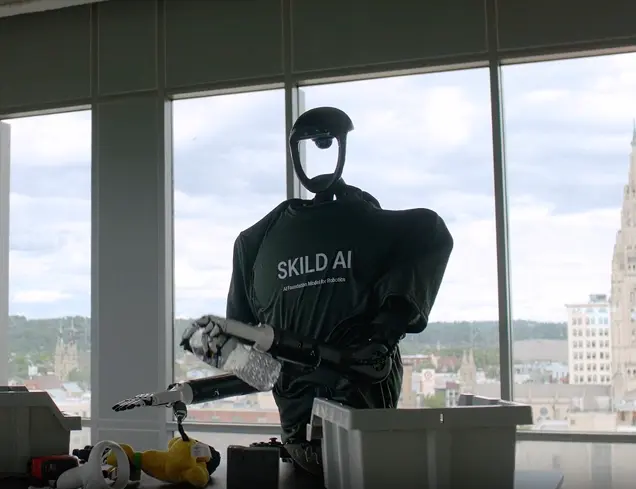 A Skild humanoid robot in a branded suit doing manipulation work by a window
