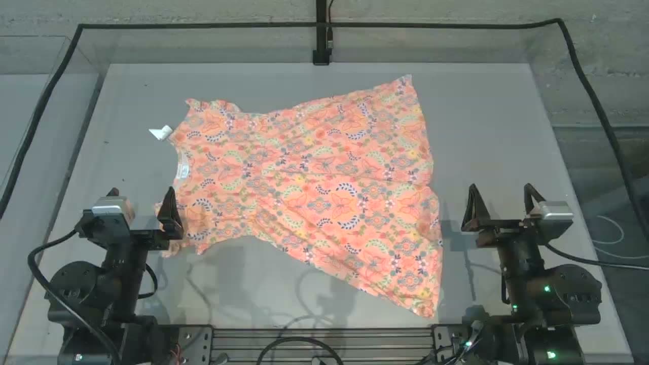 Dos brazos robóticos en un banco de pruebas doblando un vestido estampado, una de las tareas internas que Dream-1 ejecutó de forma autónoma, según Dream Labs