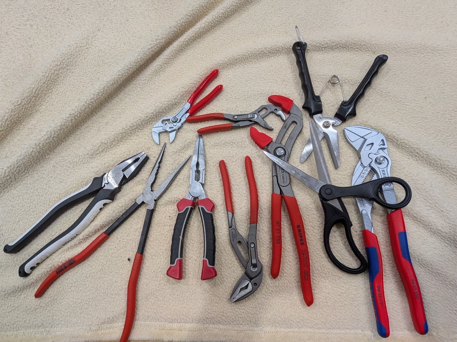 A pile of red, grey and black pliers on a cream towel, some open and some closed, mixed with two pairs of scissors, used in Elorian's counting example, as taken from Elorian